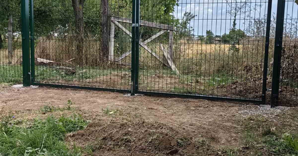 Zelena dvokrilna kapija sa panelnom ogradom na ulazu u plac